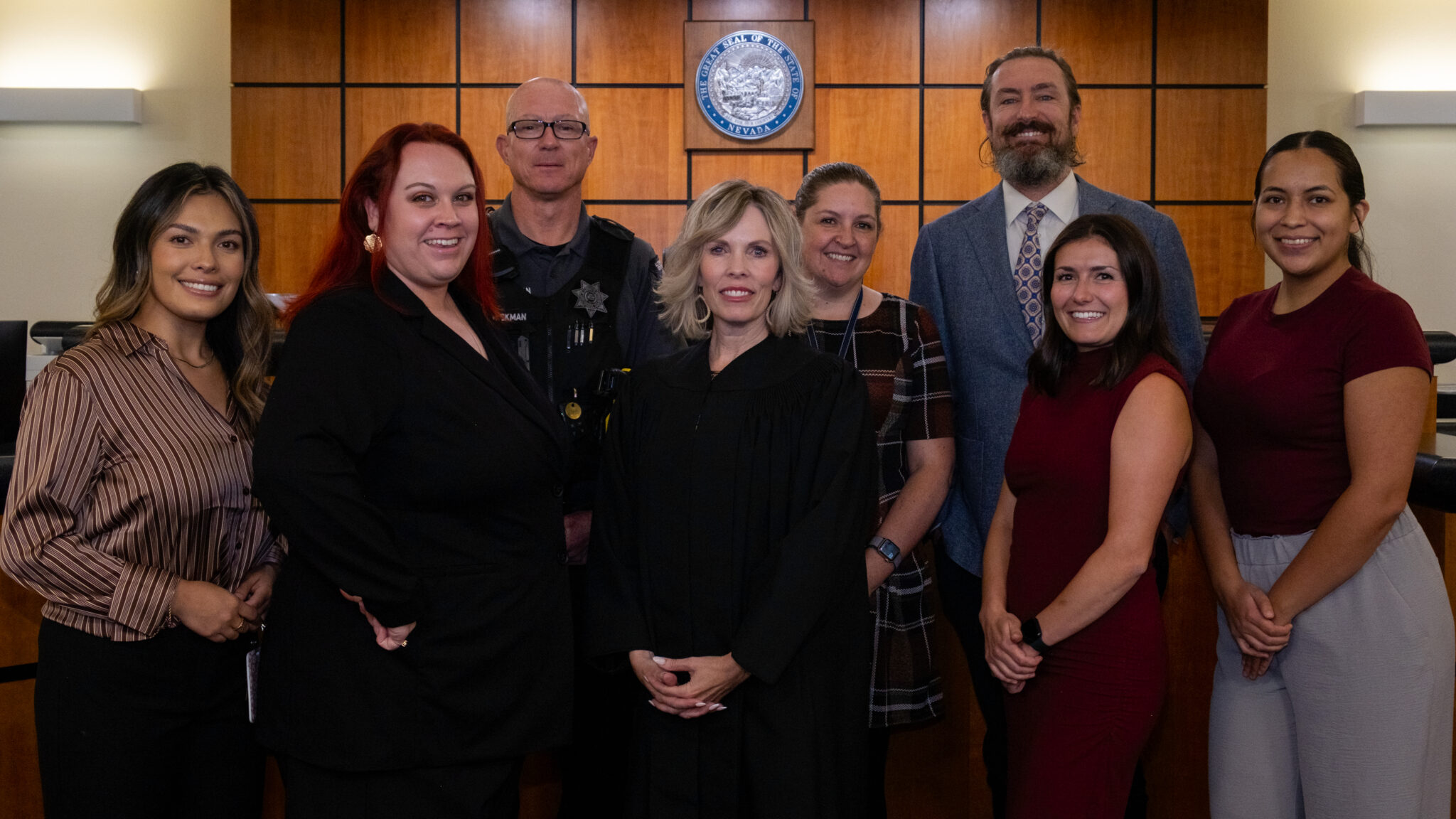 Eight people smiling at the camera with a State of Nevada seal in the background