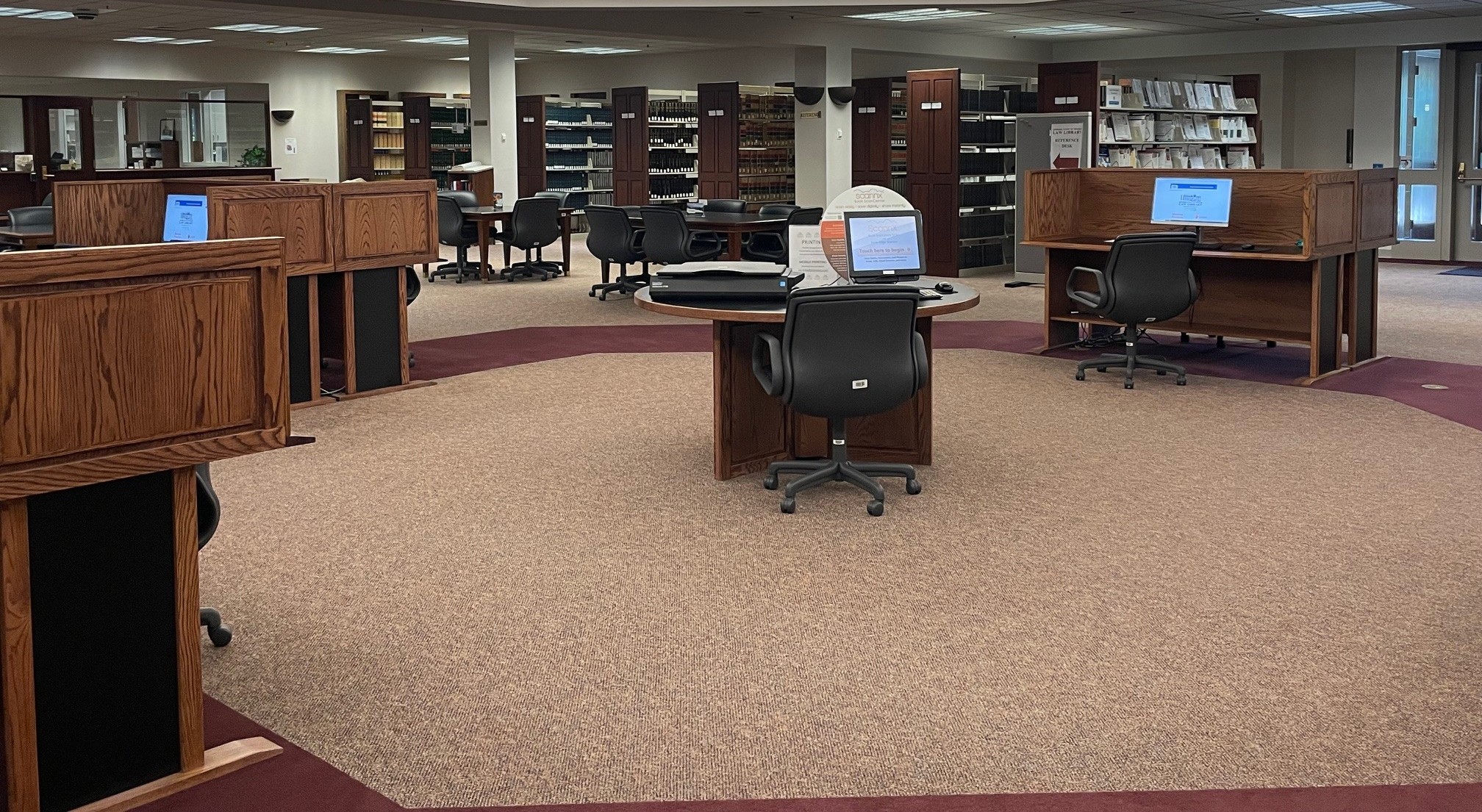 This image features carrel desks with desktop computers and a flatbed scanner. Rows of shelving units with books are visible in the background.