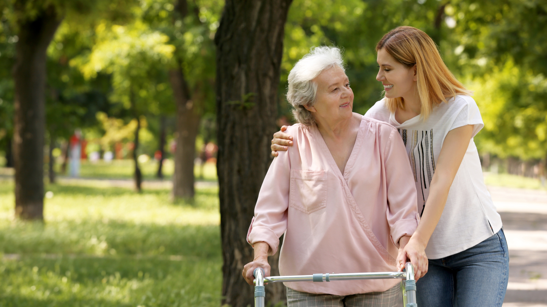 Caretaker helping elderly woman with walking frame outdoors