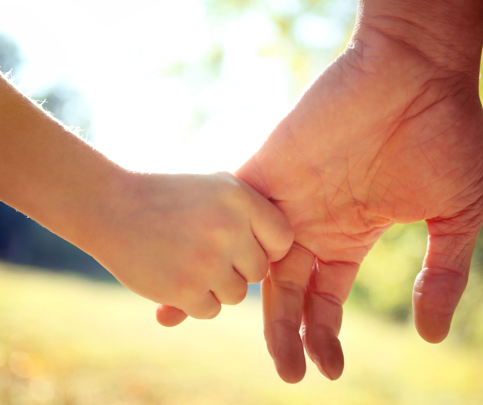 A parent holds the hand of a small child